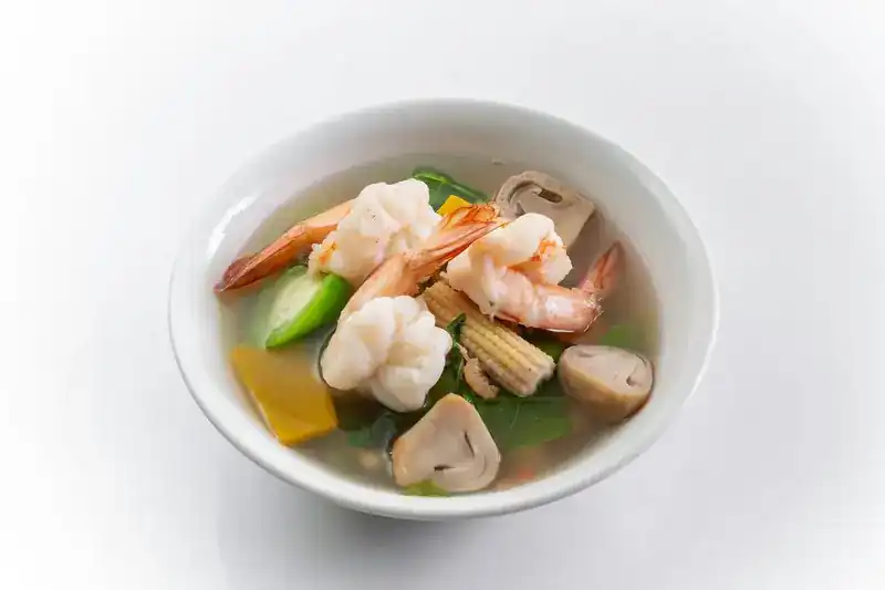 A clear soup with prawns, baby corn, mushrooms and greens