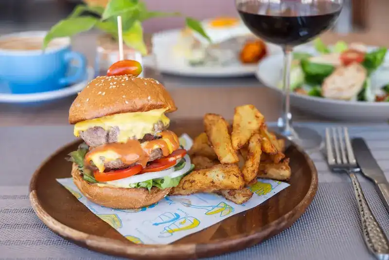 A cheeseburger with tomato and lettuce and potato wedges on the side, on a wooden plate