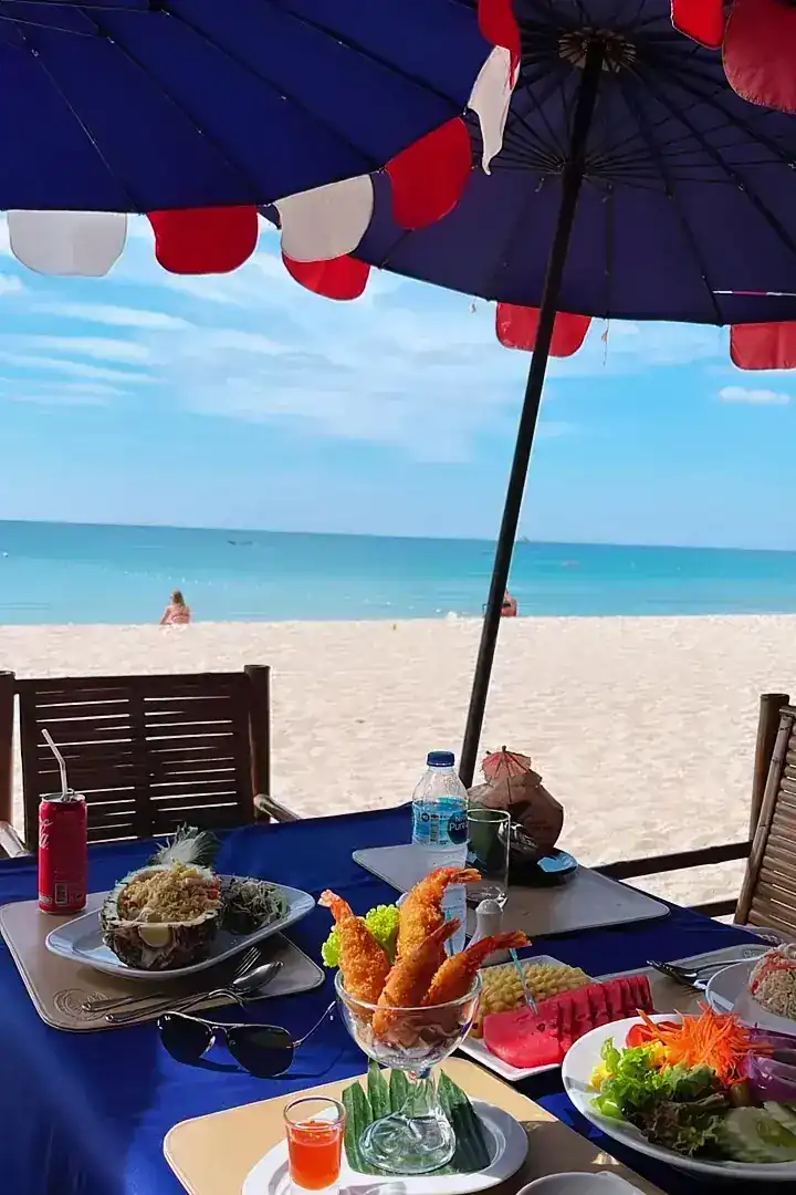 A table on the sand with fried prawns, salad and fruit, the beach and sea beyond