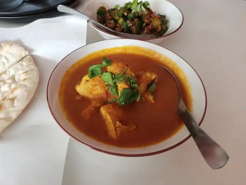 A bowl of curry with nan bread on the side