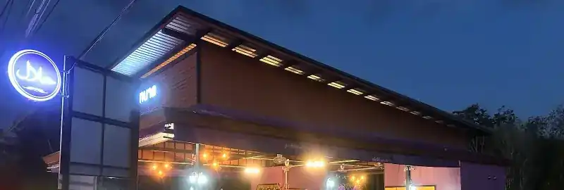 The pavilion at night, lit under its long roof, with the round halal neon sign by the road
