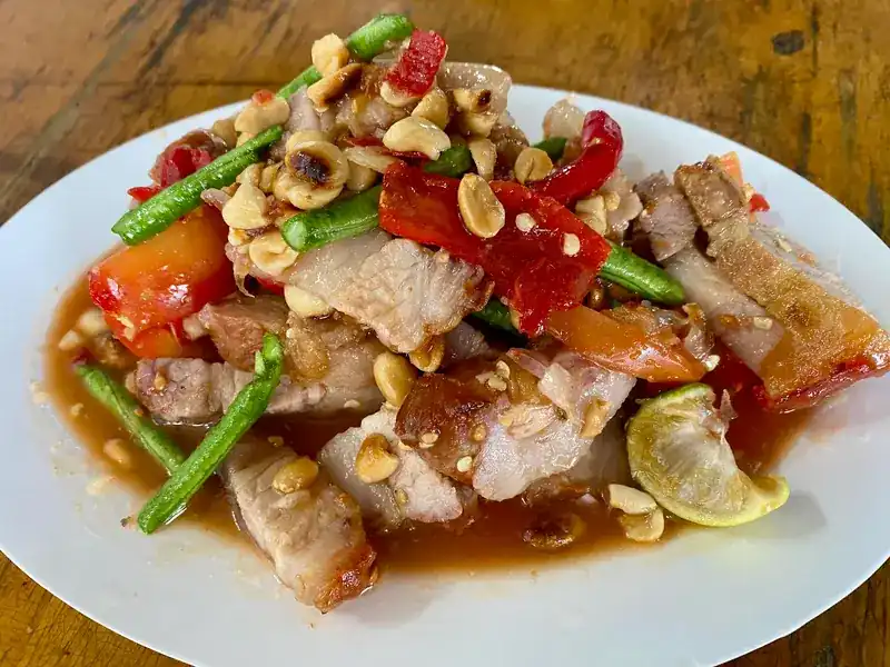 A pounded salad with crispy pork, long beans, tomato, peanuts and lime