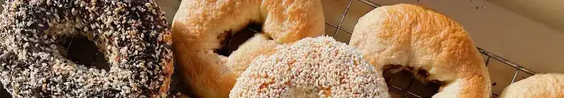 Freshly baked bagels on a wire rack, some covered in sesame and poppy seeds