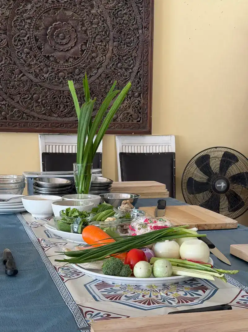 The cooking class table set with fresh vegetables, herbs, cutting boards and knives, below a carved wooden panel
