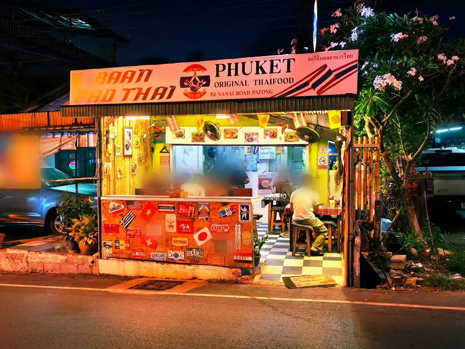 Baan Pad Thai at night on Nanai Road: the lit sign, the open shopfront and a counter covered in flags and stickers