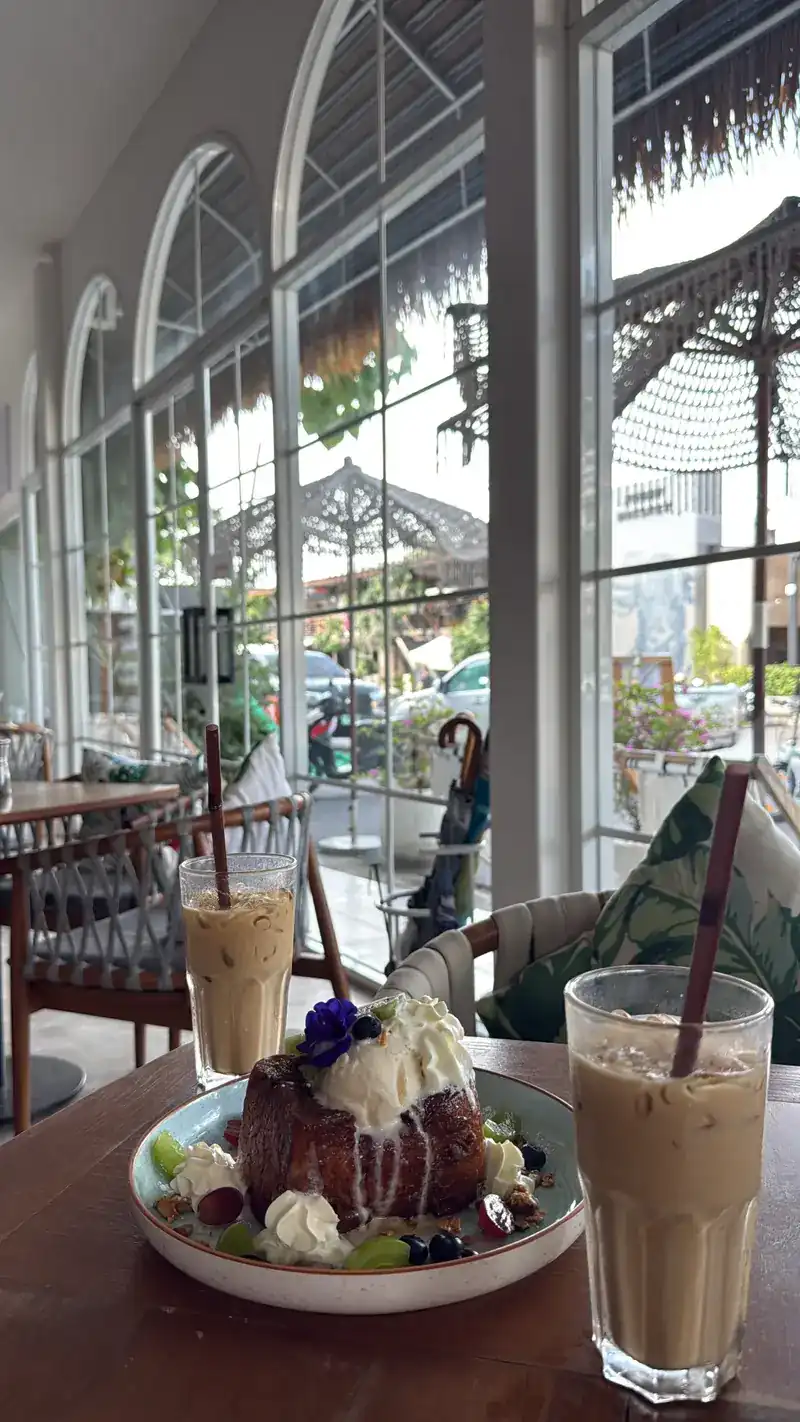 Two iced coffees and a cake with cream, berries and flowers beside the arched windows
