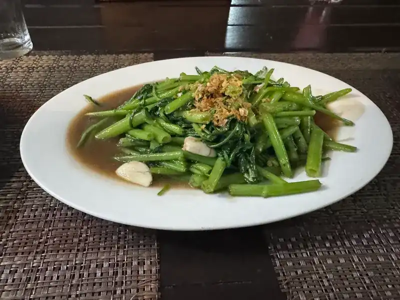 Stir-fried morning glory with garlic on a white plate / ผักบุ้งไฟแดงใส่กระเทียมในจานขาว