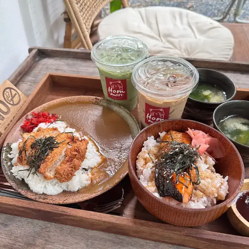 A tray with a fried cutlet on curry rice, a salmon rice bowl, soups and two iced drinks in Hommori cups