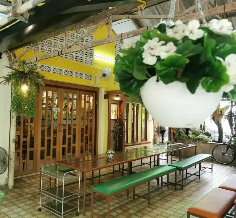 The covered terrace beside the yellow wooden house, with long tables and green benches