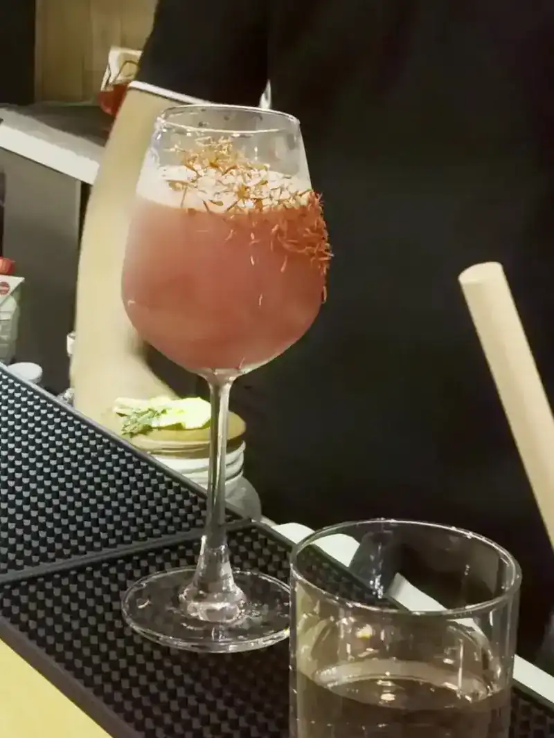 A pink drink in a wine glass on the bar