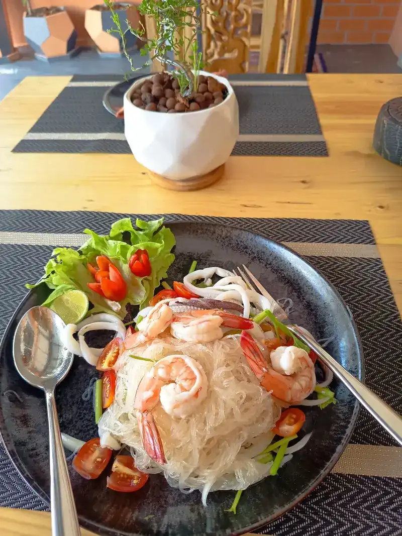 Yum woon sen seafood: glass noodle salad with prawns, tomato and lettuce on a dark plate
