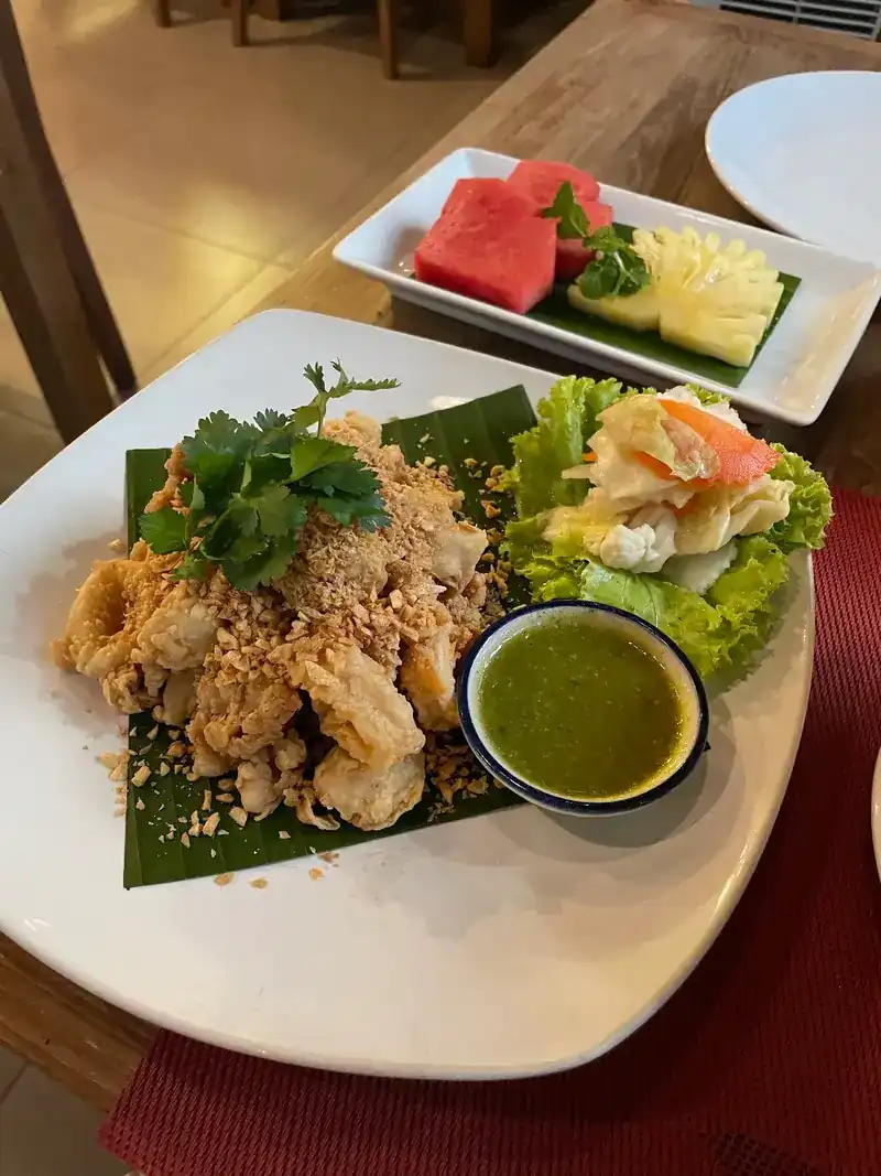 Crispy fried bites with crushed peanuts, green seafood sauce and salad, fruit plate behind