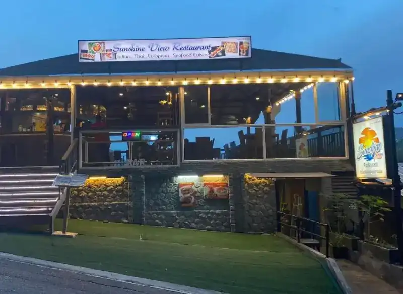 The restaurant at dusk: a lit terrace, steps up from the road and the Sunshine View sign on the roof.