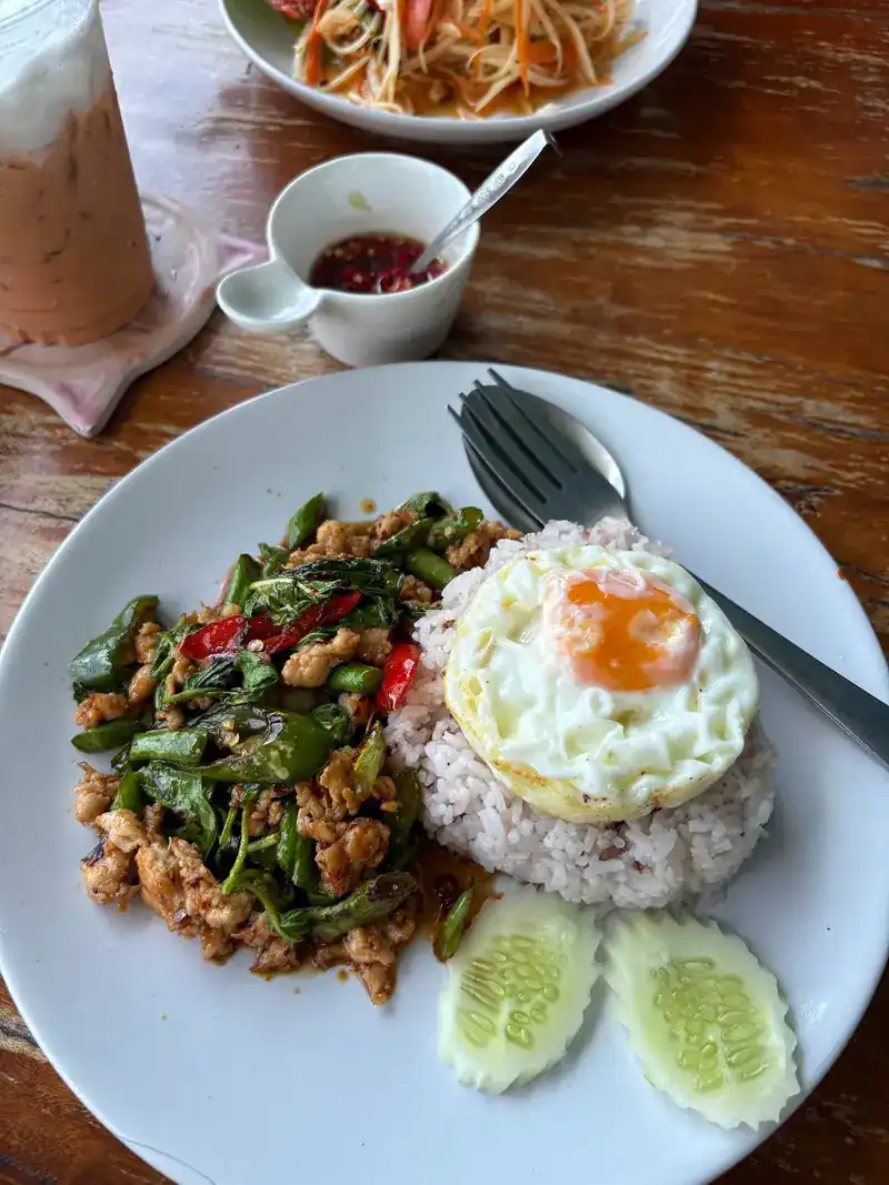 A stir-fry with long beans and red chilli beside rice topped with a fried egg and slices of cucumber