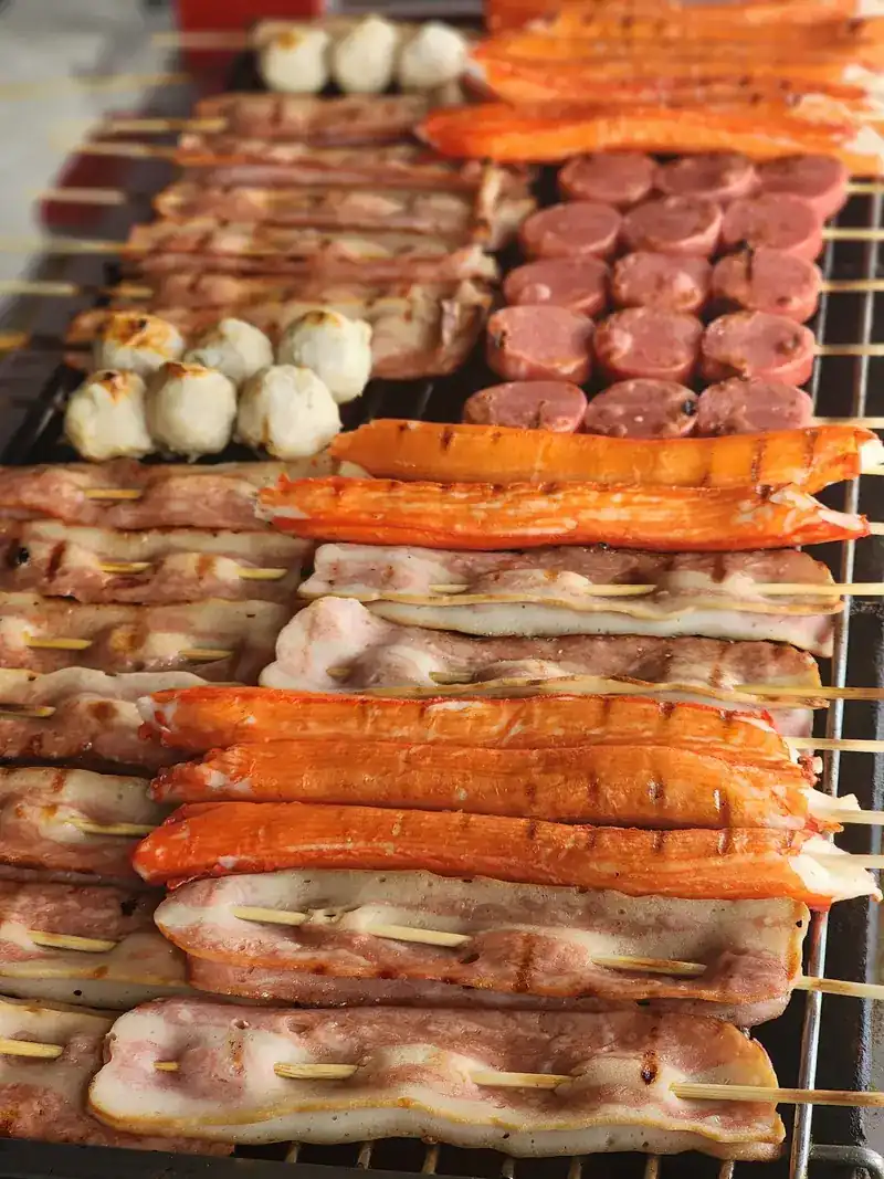 Sausages, crab sticks and meatballs on skewers over the grill