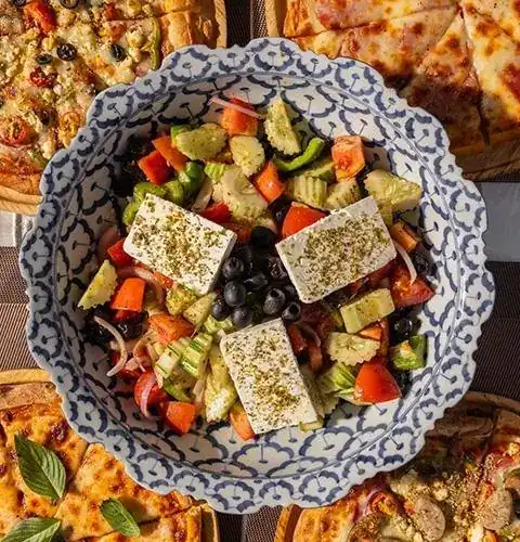 Greek salad with slabs of feta, olives and oregano in a blue and white bowl