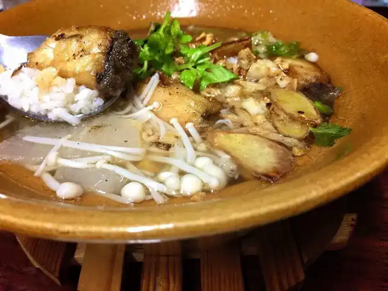 Rice soup with pieces of sea bass, ginger, mushrooms and coriander in a clay bowl