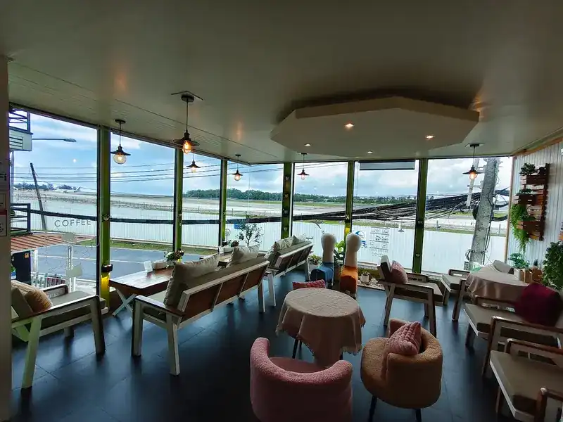 Inside the café: sofas and pink armchairs by tall windows facing the airfield