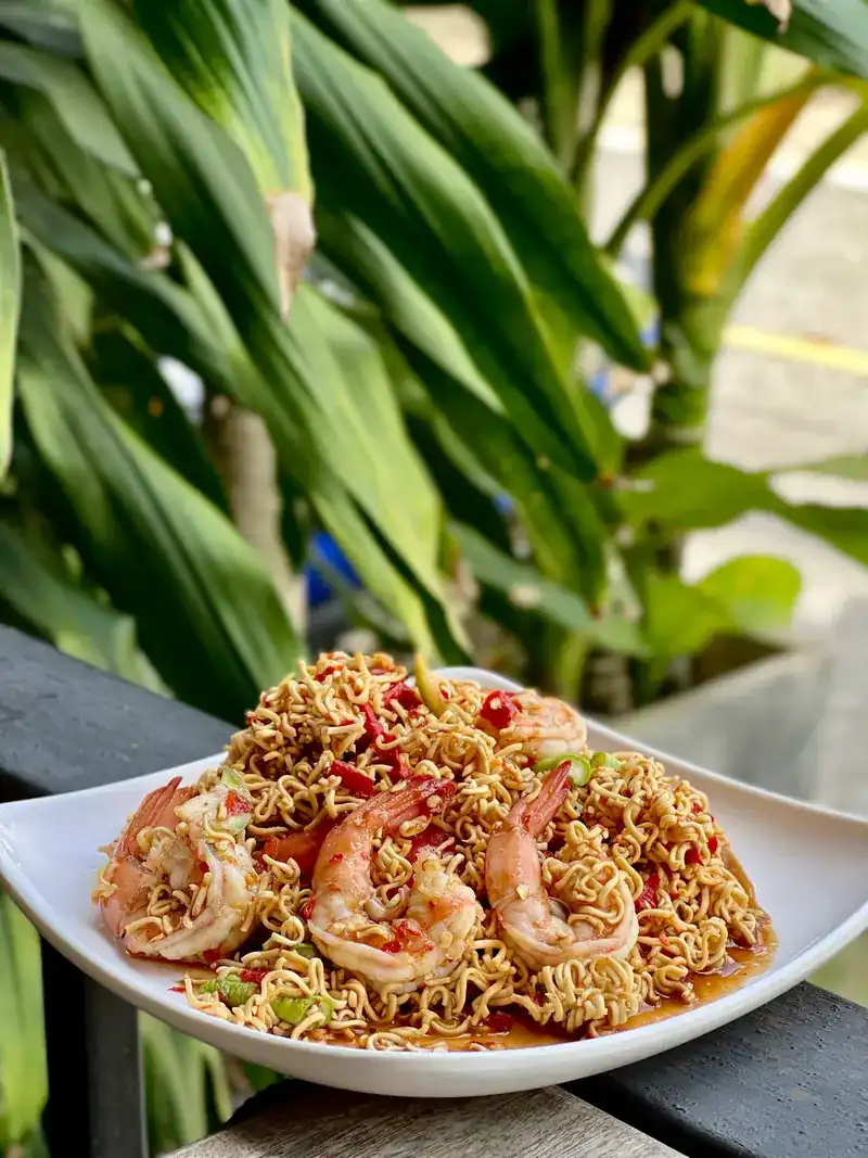 A spicy noodle salad with prawns on a white plate, green leaves behind