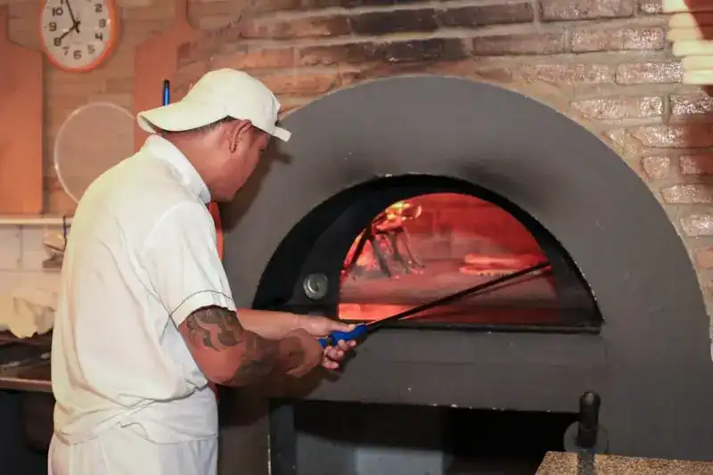 A cook, seen from behind, tending the fire in the brick wood oven
