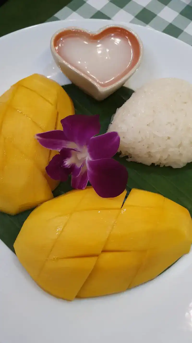 Mango sticky rice with a heart-shaped dish of coconut cream and an orchid