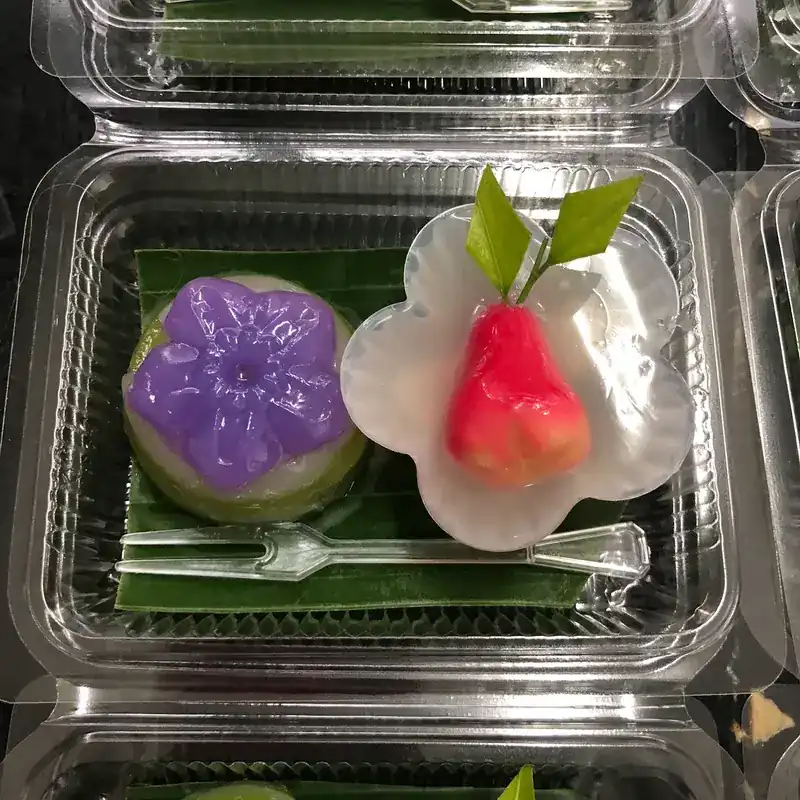 A purple flower-pressed layered sweet and a pink fruit-shaped sweet in a takeaway box