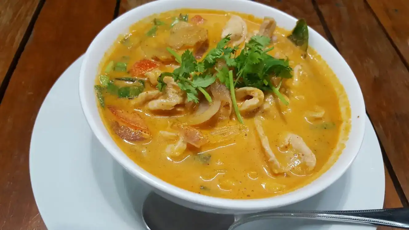 A white bowl of creamy orange soup with squid and coriander on a wooden table