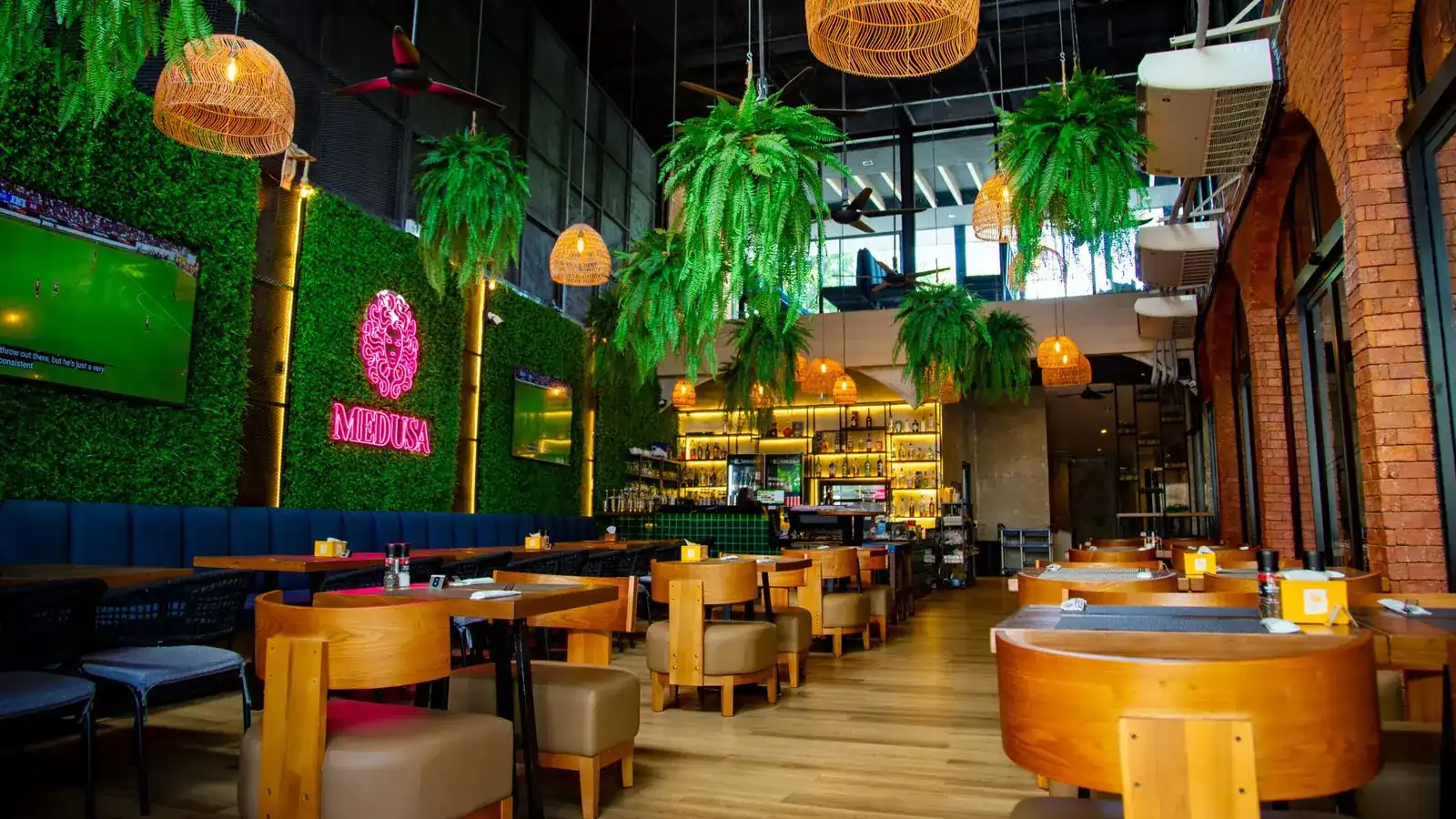 The dining room at Medusa: a pink neon Medusa sign on a wall of green leaves, hanging ferns, rattan lamps and wooden tables