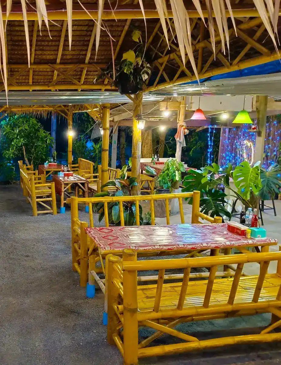 Bamboo benches and red-topped tables under a thatched roof, lit for the evening