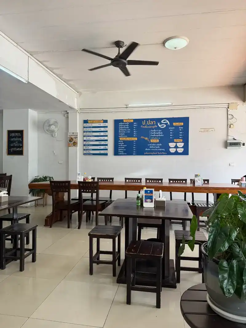The dining room: dark wooden tables and stools, a long shared table and the blue menu board on the wall