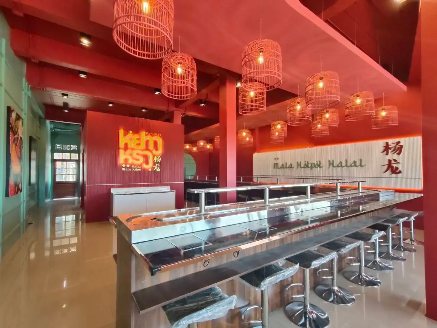 The dining room: red walls, rattan birdcage lanterns and the long steel conveyor counter lined with stools