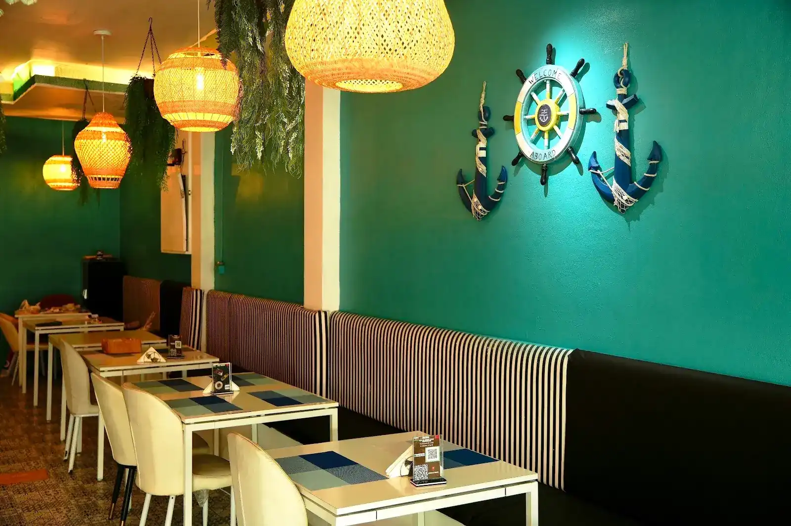 Inside BAKU: a teal wall with a ship's wheel and two anchors, rattan lamps and a long striped banquette