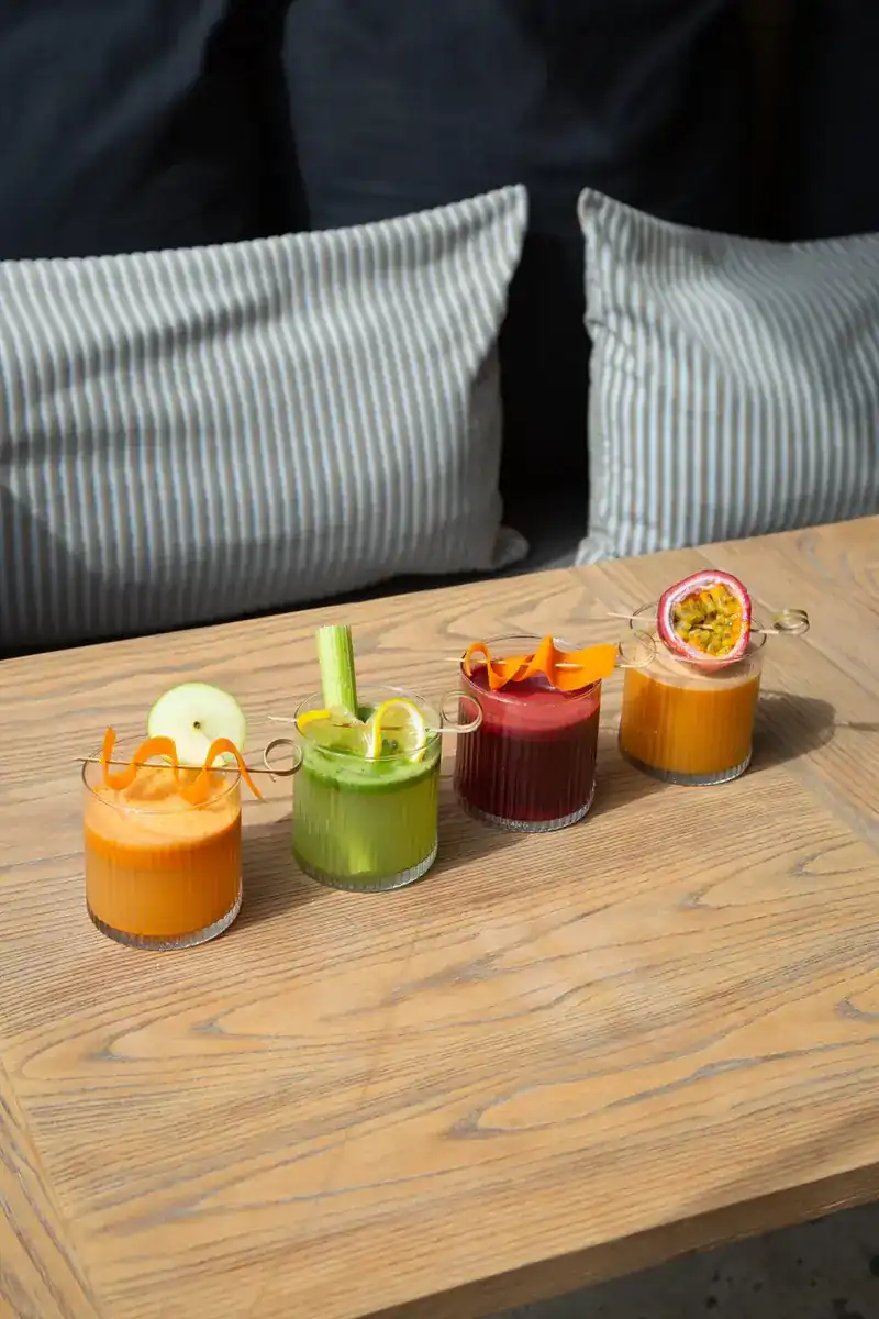 Four glasses of juice in orange, green, red and yellow on a wooden table