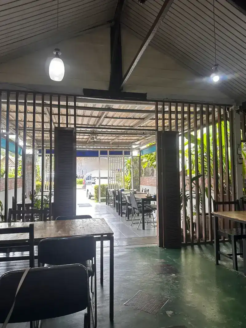 The open-sided dining room: wooden slat screens, a pitched roof, a green floor and plants outside