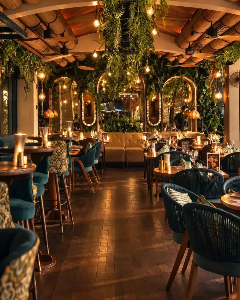 The dining room: arched mirrors, hanging ferns, teal chairs and candle-lit tables