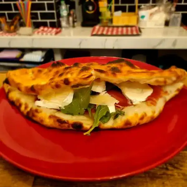 A folded calzone filled with Parma ham, mozzarella, rocket and parmesan on a red plate