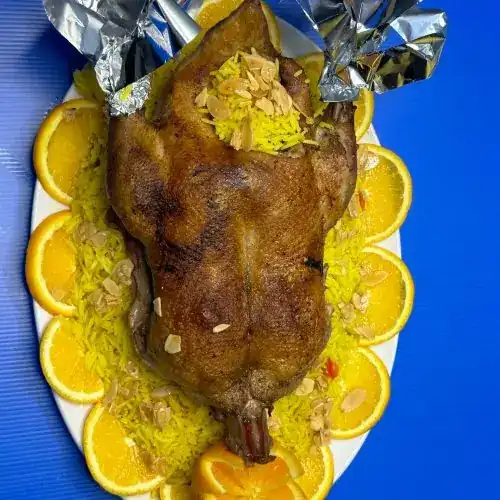A whole roast duck on yellow rice with almonds and orange slices