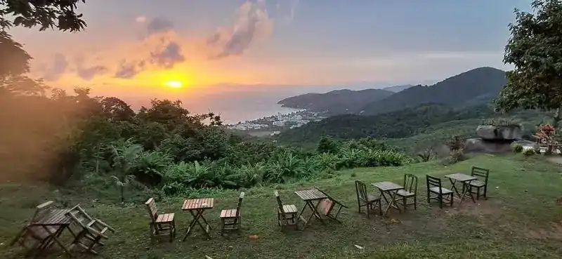 Wooden tables and chairs on the grass, set out facing the sun going down over the sea