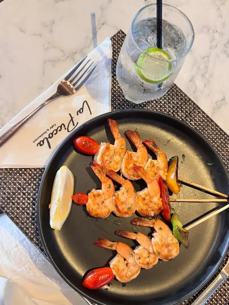 Grilled prawn skewers with cherry tomatoes and a lemon wedge on a black plate