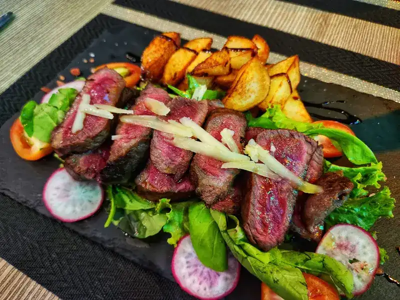 Sliced rare steak with shaved cheese, salad and roast potatoes on slate
