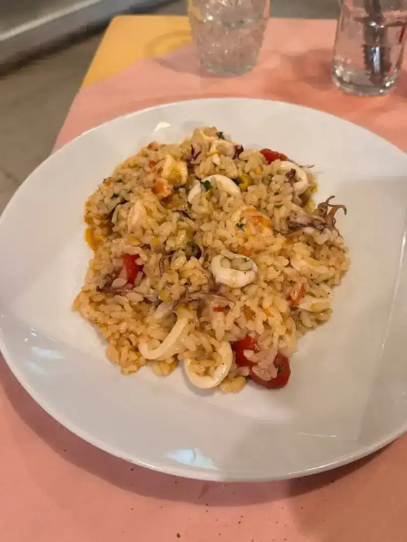 A plate of rice with squid and tomato on a pink tablecloth