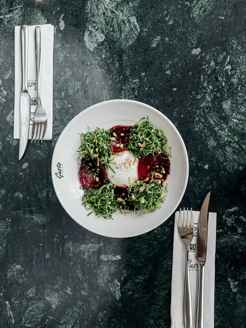A salad of beetroot, greens and soft white cheese on a Gusto plate, seen from above on green marble