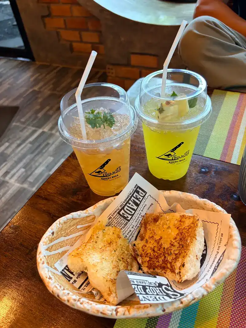 Two homemade mocktails in cups printed with the restaurant's logo, and a basket of garlic bread