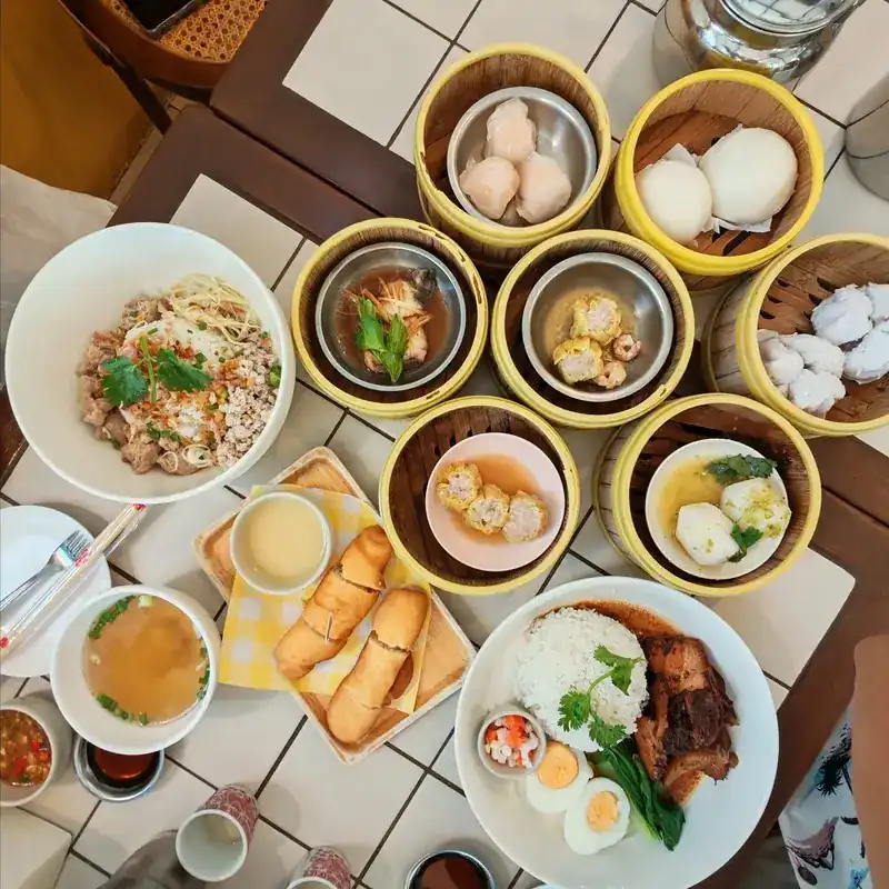 A table of dim sum steamers, noodles, fried dough sticks with a dip, and braised pork on rice with egg