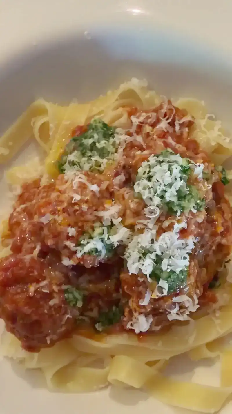 Ribbon pasta with meatballs in tomato sauce, topped with grated cheese and herbs