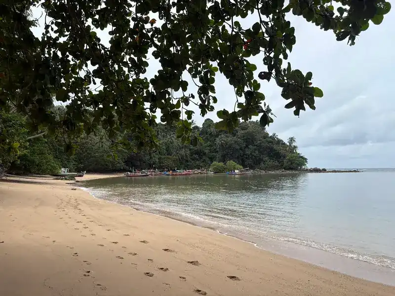 A quiet stretch of sand with footprints, and longtail boats moored in the bay