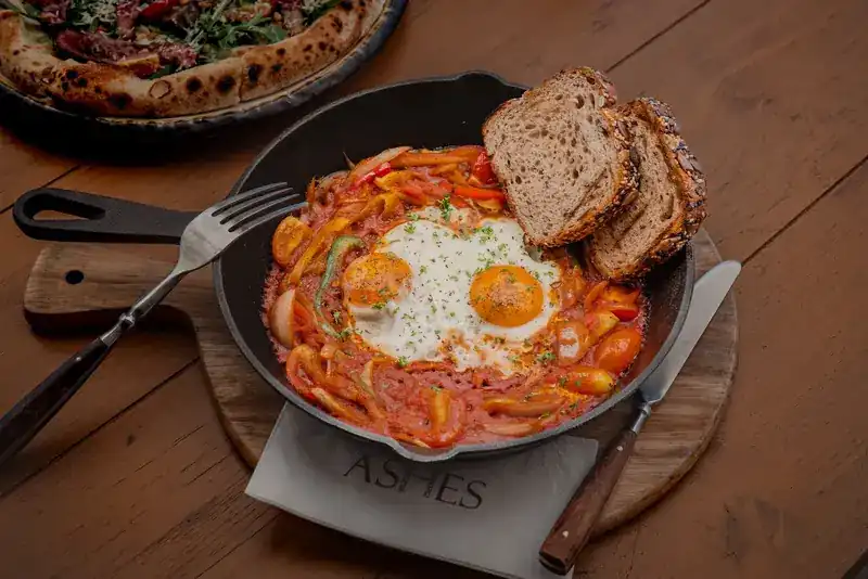 Eggs cooked in tomato and peppers in an iron pan, with toasted bread