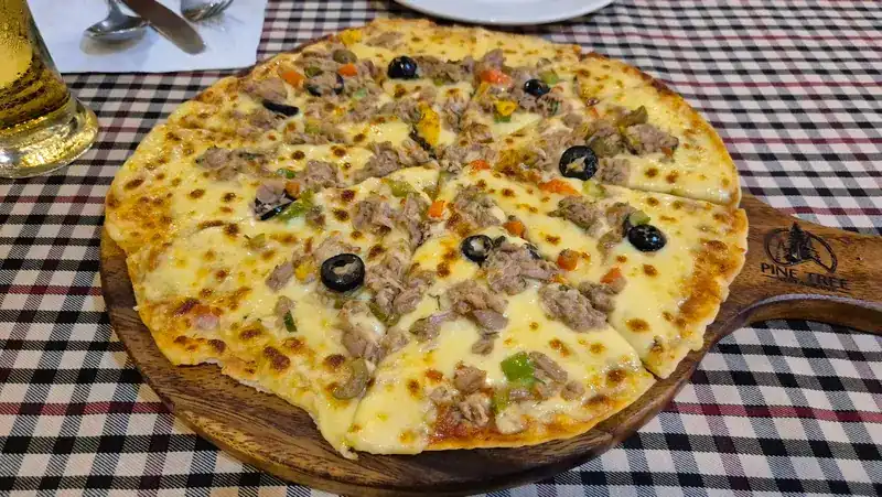 A pizza with cheese, olives and peppers on a wooden board branded Pine Tree