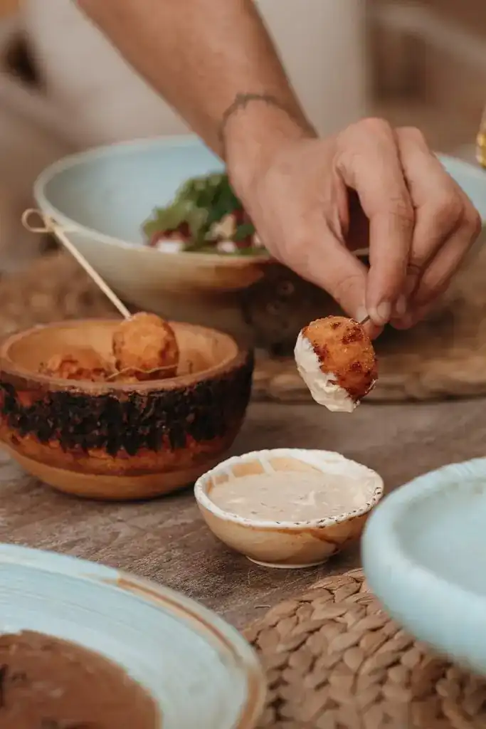 A hand dipping a fried cheese ball into a creamy sauce