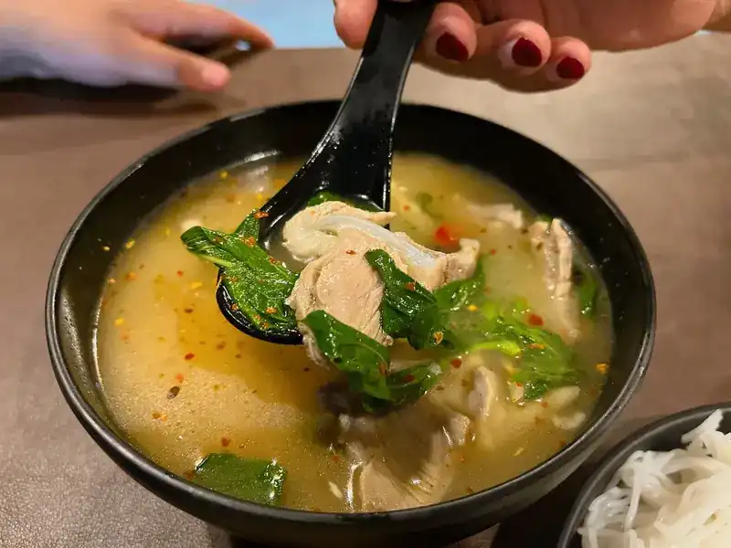 A spoonful of spicy soup with tender meat and green leaves